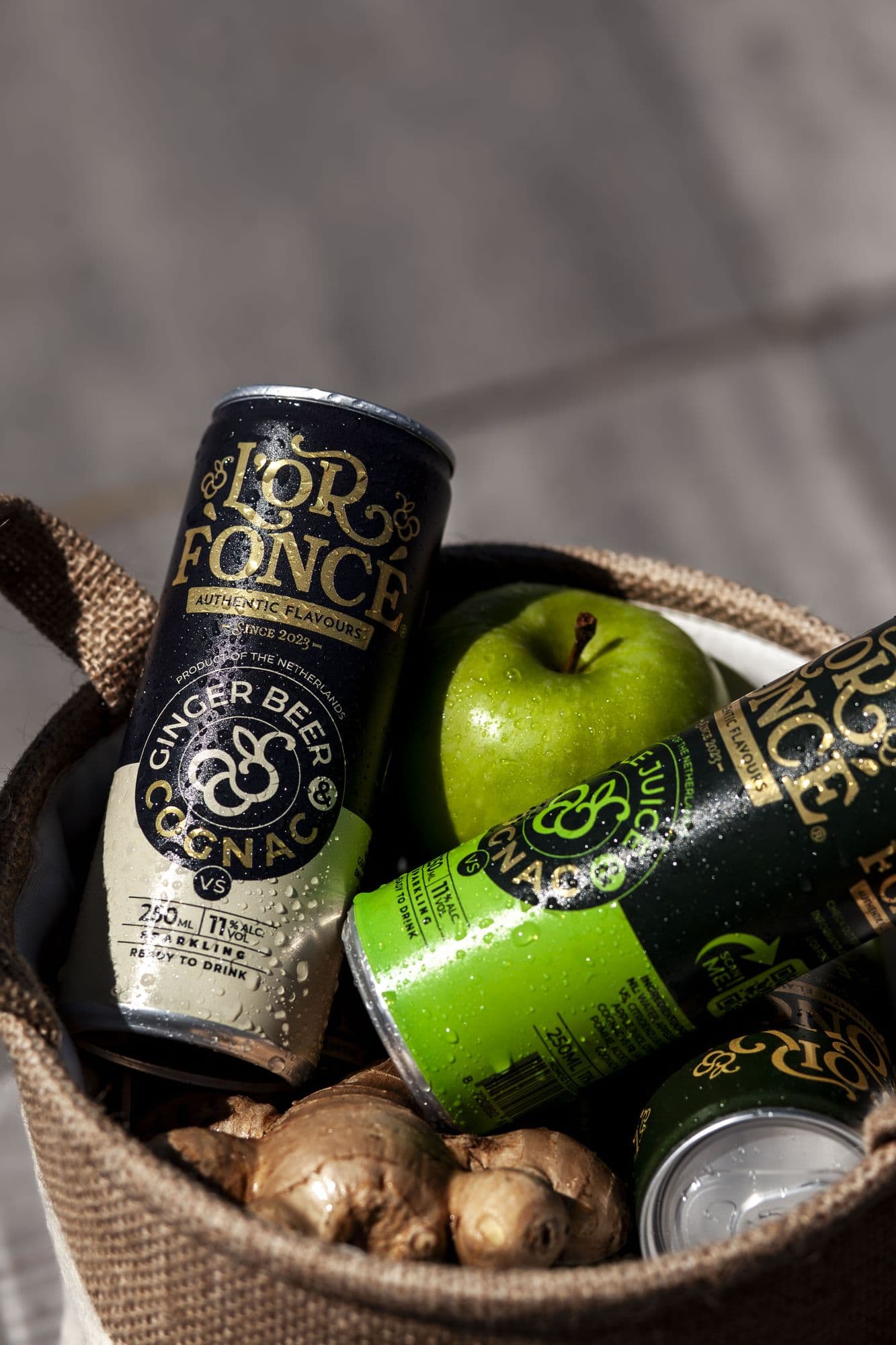 Drinks cans in a basket with a green apple and ginger
